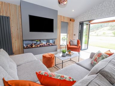 A living room with a grey sofa orange cushions an orange chair and ottoman a marble coffee table and a wall mounted TV at Pool View in Meifod Powys