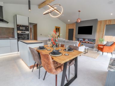 A dining table set with black bowls and glasses in an open plan living area with kitchen appliances a grey sofa and an orange armchair at Pool View in Meifod Powys