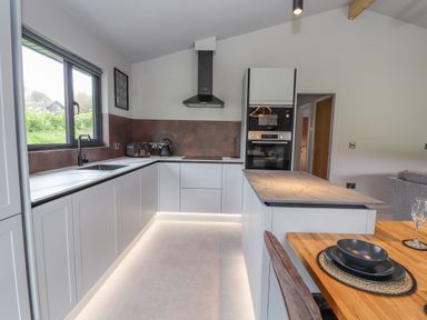 A kitchen with white cabinets a black sink and window a wooden dining table with black dishes at Pool View in Meifod Powys