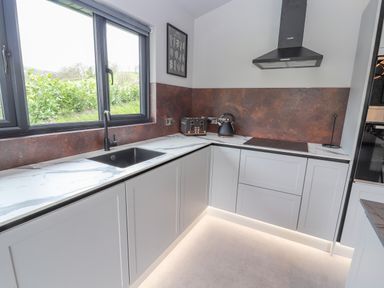 A kitchen with a black sink under a window a toaster kettle and stovetop at Pool View in Meifod Powys