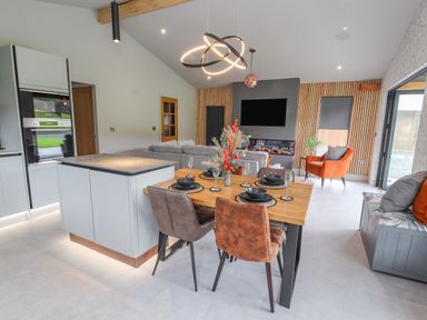 A dining area with table set for four near a kitchen island and a living room with a television and fireplace at Pool View in Meifod Powys