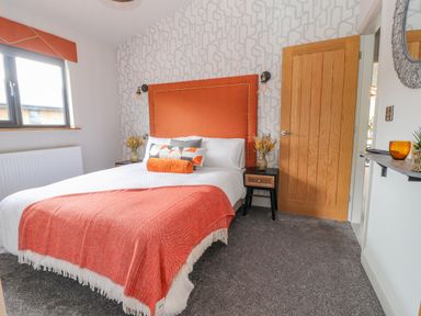 A bedroom with a double bed with orange headboard and throw at Pool View in Meifod Powys