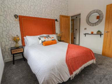 A bedroom with an orange headboard white bedding orange throw blanket and pillows beside wooden doors and a wall mirror at Pool View in Meifod Powys