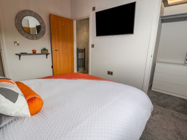 A bedroom with a bed a wall-mounted television a wooden door a round mirror a small shelf with decor and an open closet with drawers at Pool View in Meifod Powys