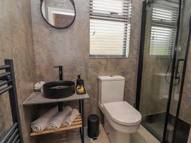A bathroom with a black round sink on a marble countertop a white toilet a window with blinds and a glass shower enclosure at Pool View in Meifod Powys