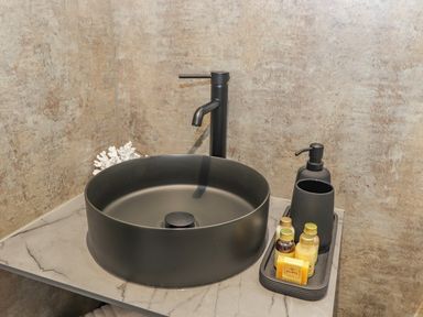 A bathroom sink with a black faucet a soap dispenser toiletries and a cup on a countertop at Pool View in Meifod Powys