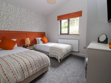 A bedroom with two single beds orange headboards and pillows a patterned wall and a window at Pool View in Meifod Powys