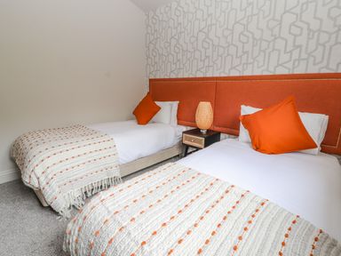 A bedroom with two single beds with orange headboards pillows and patterned blankets at Pool View in Meifod Powys