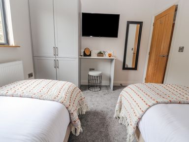 A bedroom with two beds a white wardrobe a wall mounted tv a small desk with a stool and a mirror at Pool View in Meifod Powys