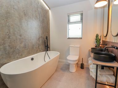 A bathroom with a freestanding bathtub toilet two black sinks with mirrors and rolled towels at Pool View in Meifod Powys