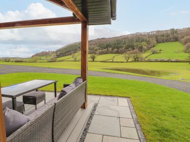 An outdoor seating area with a table and chairs overlooking green fields and a small pond at Pool View in Meifod Powys