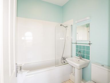 A bathroom with a bathtub shower combination a sink with a mirror above and a toilet at Plas Newydd Llanfaelog near Rhosneigr