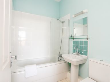 A bathroom with a bathtub shower combination a sink a mirror and a toilet at Plas Newydd in Llanfaelog near Rhosneigr