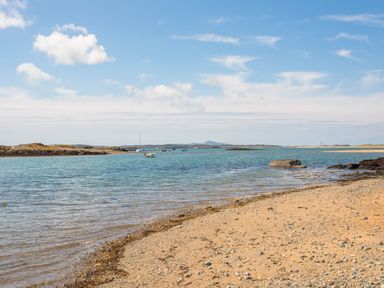A sandy and rocky beach with calm water and several small boats near the shore at Plas Newydd Llanfaelog near Rhosneigr
