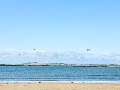 A beach with a sea and kitesurfing kites in the water at Plas Newydd in Llanfaelog near Rhosneigr