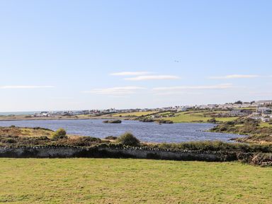A landscape with a river a stone wall grassy fields and houses in the distance at Plas Newydd Llanfaelog near Rhosneigr