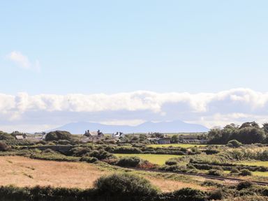 A rural landscape with fields bushes houses and mountains in the background at Plas Newydd in Llanfaelog near Rhosneigr