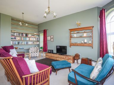 A living room with bookshelves chairs and a television at Plas Newydd in Llanfaelog near Rhosneigr