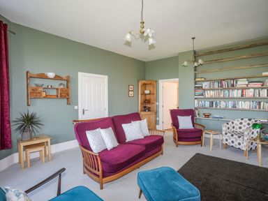 A living room with purple and blue chairs a bookshelf and wooden furniture at Plas Newydd in Llanfaelog near Rhosneigr