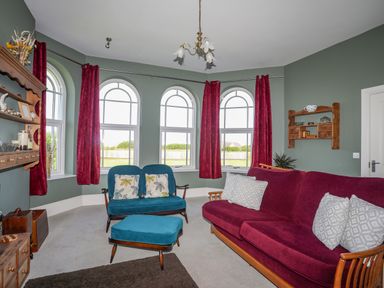 A sitting room with blue and purple upholstered chairs and arched windows at Plas Newydd Llanfaelog near Rhosneigr