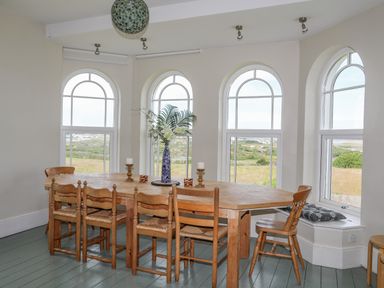 A dining room with a wooden table and chairs and arched windows at Plas Newydd in Llanfaelog near Rhosneigr