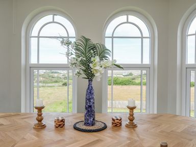 A wooden table with a blue vase of flowers two wooden candle holders and two small wooden boxes in front of arched windows at Plas Newydd Llanfaelog near Rhosneigr