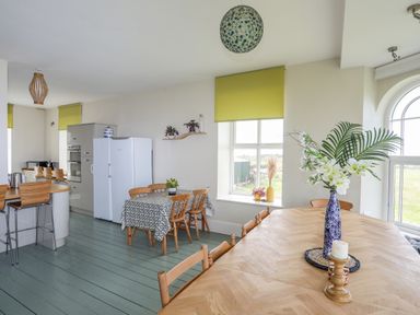A kitchen and dining area with wooden chairs tables and green window blinds at Plas Newydd Llanfaelog near Rhosneigr