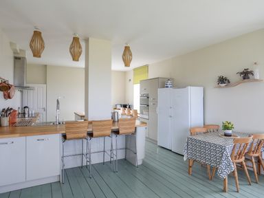 A kitchen with wooden stools at a counter white cabinets and appliances and a dining table with chairs at Plas Newydd Llanfaelog near Rhosneigr