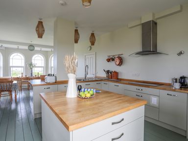 A kitchen with a wooden countertop island and dining area with wooden chairs and arched windows at Plas Newydd Llanfaelog near Rhosneigr