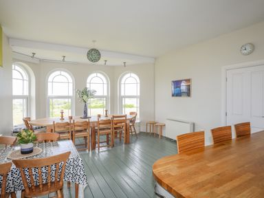 A dining room with wooden tables and chairs near arched windows at Plas Newydd Llanfaelog near Rhosneigr