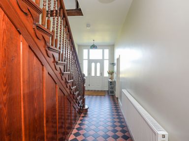 A hallway with wooden staircase black and red checkered tile floor white door and radiator at Plas Newydd in Llanfaelog near Rhosneigr