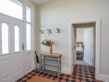 An entryway with a white front door a shoe rack with a flower vase and hooks on the wall at Plas Newydd in Llanfaelog near Rhosneigr