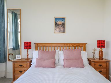 A bedroom with a wooden bed frame two red lamps on wooden nightstands and a mirror at Plas Newydd in Llanfaelog near Rhosneigr