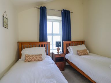 A bedroom with two single beds a small wooden bedside table with a lamp and a window with blue curtains at Plas Newydd in Llanfaelog near Rhosneigr