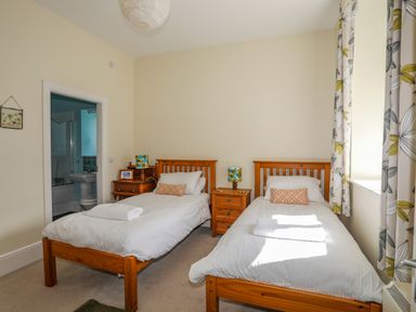 A bedroom with two single wooden beds a bedside table with lamps and a window with floral curtains at Plas Newydd Llanfaelog near Rhosneigr