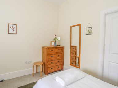 A bedroom corner with a wooden chest of drawers stool mirror and bed with towel at Plas Newydd Llanfaelog near Rhosneigr