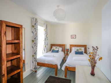 A bedroom with two single beds a wooden shelf and a table with a vase of flowers at Plas Newydd in Llanfaelog near Rhosneigr