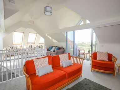 A sitting area with two orange couches and a glass door leading to an outdoor balcony at Plas Newydd in Llanfaelog near Rhosneigr