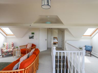 A landing area with orange sofas a patterned armchair a small wooden table a blue cushioned chair skylights and a staircase at Plas Newydd in Llanfaelog near Rhosneigr