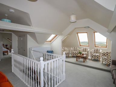 An upper floor landing area with a white wooden railing and six polka dot chairs around a wooden table by angled windows at Plas Newydd in Llanfaelog near Rhosneigr