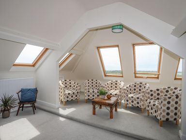 An attic seating area with five polka dot armchairs around a wooden table and a window with a green lampshade at Plas Newydd in Llanfaelog near Rhosneigr