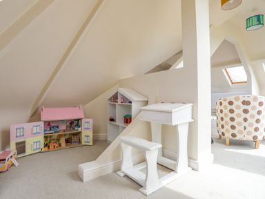 A playroom with a dollhouse and white children's desk and stool at Plas Newydd in Llanfaelog near Rhosneigr