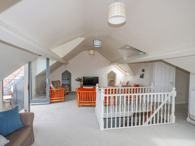 An attic living room with armchairs a television and a staircase at Plas Newydd in Llanfaelog near Rhosneigr