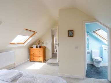 A bedroom with a wooden chest of drawers next to a window and an adjoining bathroom with a toilet at Plas Newydd in Llanfaelog near Rhosneigr