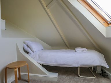 A small bedroom with a single bed under a slanted ceiling next to a wooden stool at Plas Newydd in Llanfaelog near Rhosneigr
