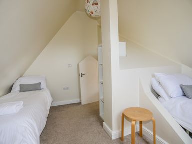 A bedroom with two single beds a small stool a small door and built-in shelving at Plas Newydd in Llanfaelog near Rhosneigr