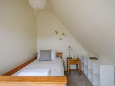 A small bedroom with a single wooden bed side table a lamp and a white shelving unit at Plas Newydd Llanfaelog near Rhosneigr