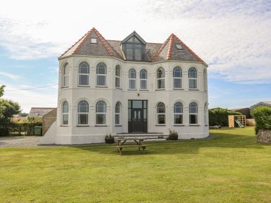 A large white house with arched windows and a lawn with a picnic table at Plas Newydd Llanfaelog near Rhosneigr