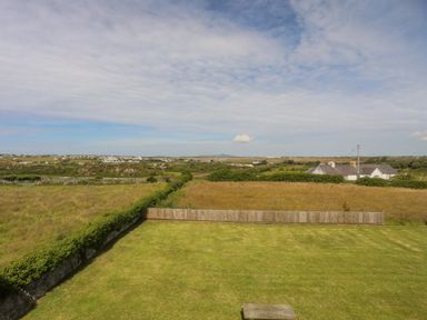 A grassy yard with a wooden fence and open fields with houses in the distance at Plas Newydd in Llanfaelog near Rhosneigr