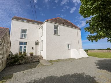A white two-story house with multiple windows next to a tree and grassy area at Plas Newydd in Llanfaelog near Rhosneigr
